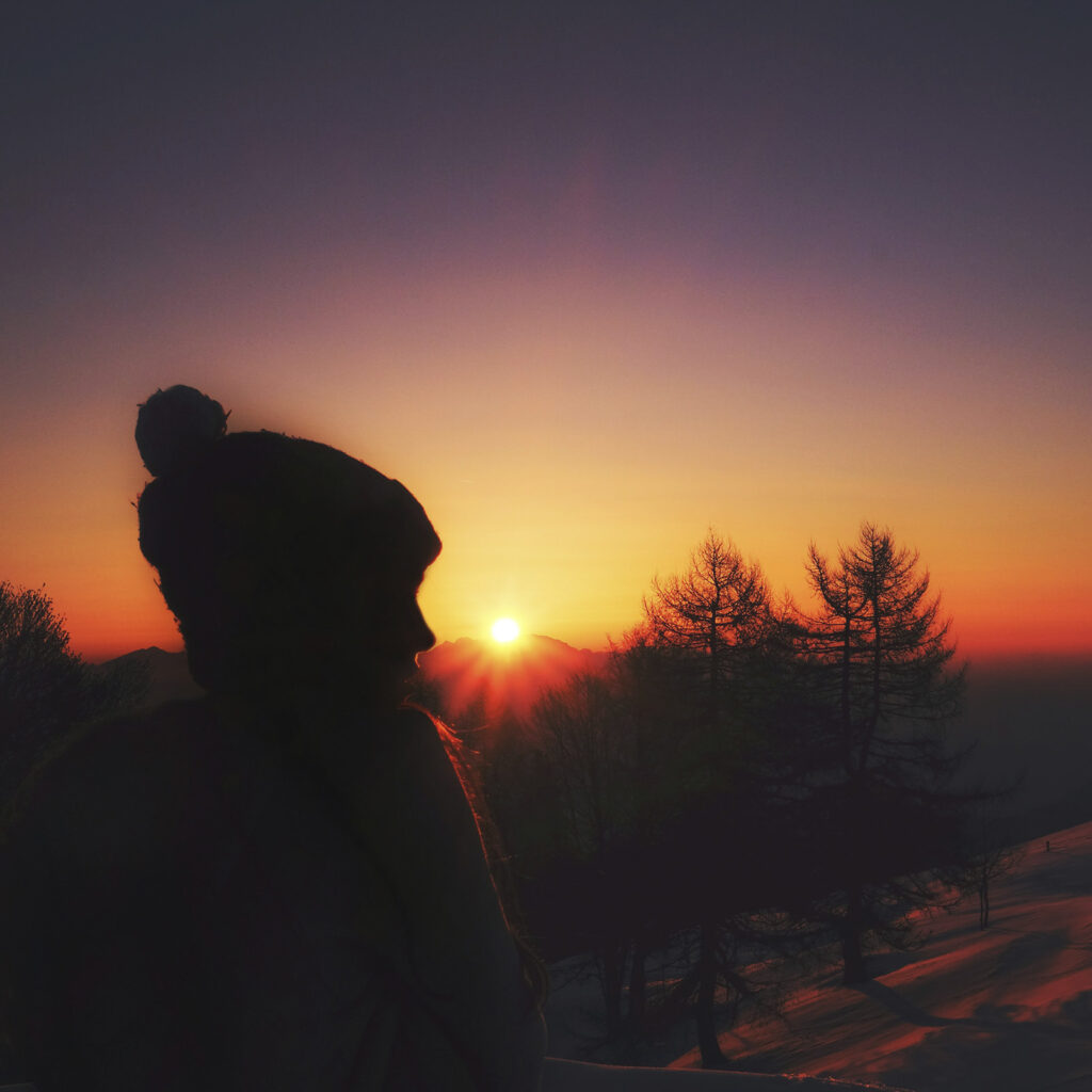 Sonnenaufgang über verschneiter Landschaft mit weiblicher Silhouette im Gegenlicht als Symbol für Schwelle und Neubeginn.