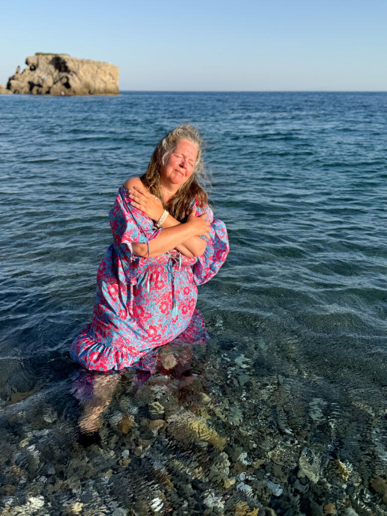 Claudia Korsten-Ring steht im flachen Meer und hält sich mit überkreuzten Armen selbst.