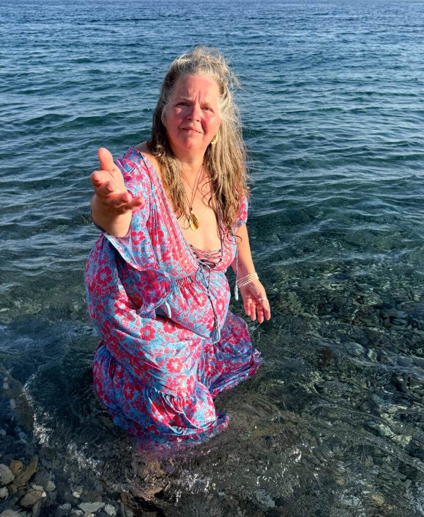 Claudia Korsten-Ring steht im Meer und streckt der Betrachterin einladend die Hand entgegen.